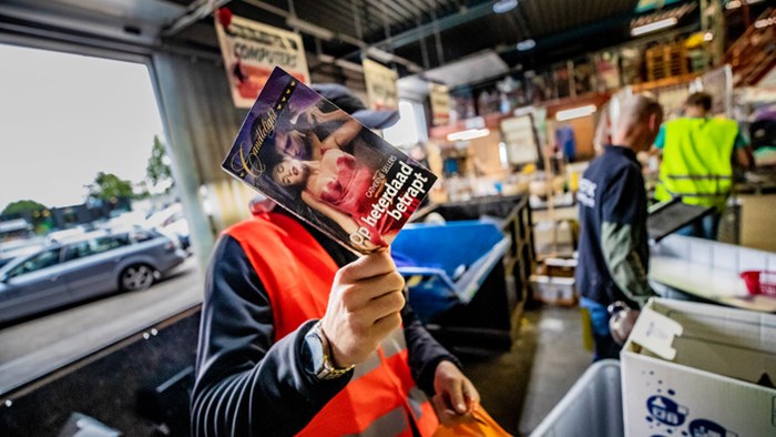 Een van de taakstraffers laat een boek zien dat is ingeleverd bij kringloop Foenix in Apeldoorn. © Rob Voss