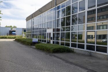 Werkstraflocatie van Reclassering Nederland aan de Computerweg in Utrecht. Een gebouw met veel glas en in het midden een bewegwijzeringsbordje met daarop Reclassering Nederland en het logo.