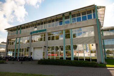 Werkstraflocatie aan de Gyroscooopweg in Amsterdam. Een verzamelgebouw op een industrieterrein met veel spiegelend glas. Bovenop een groen logo van Maarif Europe.