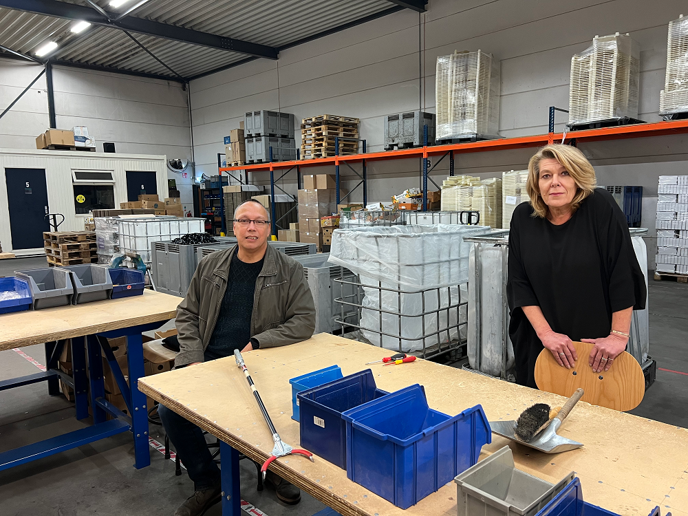 mannelijke collega zittend en vrouwelijke collega staand, beide aan een werktafel