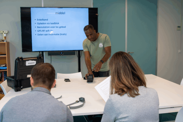 Donkerkleurige reclasseringswerker in een ruimte met twee andere reclasseringswerkers die praten over de enkelband tijdens een training