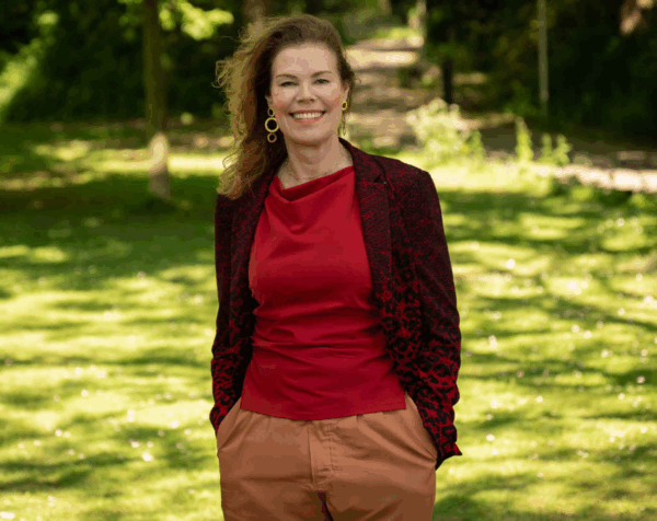 directielid Jessica Westerik in park, gekleed in een rode jurk met print.