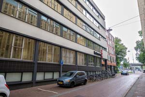 hoog flatgebouw langs de weg, met parallel geparkeerde auto's