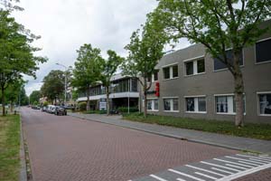 wit grijs kantoorpand met 2 verdiepingen, waarop het Reclassering Nederland-logo zichtbaar is boven het raam, langs een autoweg