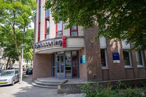 Gebouw met een ronde hoek, met rode accenten op de langwerpige ramen, omringd door bomen