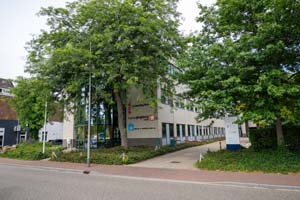 drie logo's, waaronder reclassering nederland, bureau jeugdzorg en noord en midden limburg, op een gebouw met reflecterend glas aan de linkerkant, met een voetenpad omringd door bomen en gras